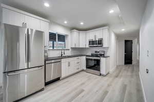 Kitchen with white cabinetry, stainless steel appliances, light hardwood / wood-style floors, and sink