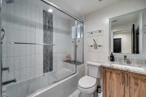 Full bathroom featuring toilet, vanity, and shower / bath combination with glass door