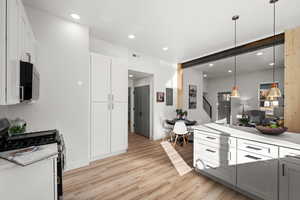 Kitchen featuring white cabinetry, stainless steel range with gas cooktop, light hardwood / wood-style flooring, and decorative light fixtures