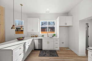 Kitchen with sink, light hardwood / wood-style flooring, dishwasher, white cabinetry, and hanging light fixtures