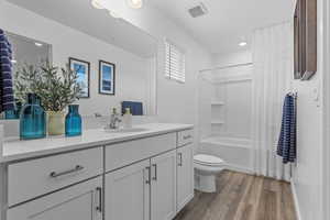 Full bathroom with toilet, wood-type flooring, shower / bathtub combination with curtain, and vanity