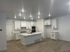 Kitchen featuring built in microwave, sink, white cabinetry, stainless steel oven, and an island with sink