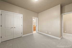 Unfurnished bedroom with light colored carpet, a textured ceiling, ensuite bath, and a closet