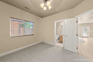 Unfurnished bedroom with ensuite bathroom, light tile patterned floors, and ceiling fan