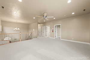 Carpeted spare room with ceiling fan with notable chandelier