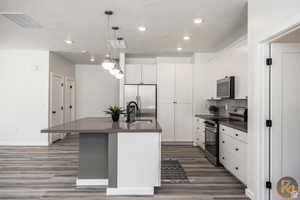 Kitchen with appliances with stainless steel finishes, sink, white cabinets, hanging light fixtures, and a center island with sink