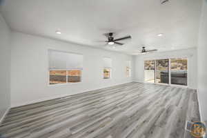 Unfurnished living room featuring ceiling fan, a wealth of natural light, a textured ceiling, and light wood-type flooring