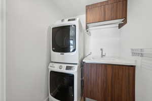 Washroom featuring stacked washer and dryer, sink, and cabinets