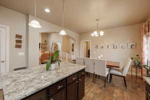 Kitchen with hanging light fixtures, hardwood / wood-style flooring, a center island, and dark brown cabinets