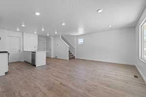 Unfurnished living room with sink, a wealth of natural light, light hardwood / wood-style flooring, and a textured ceiling