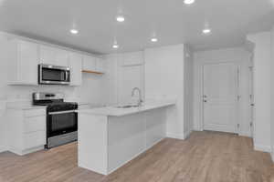 Kitchen with white cabinetry, sink, kitchen peninsula, stainless steel appliances, and light wood-type flooring