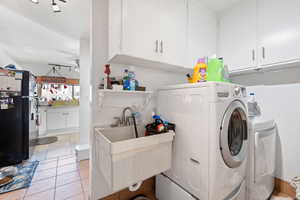 Laundry room featuring light tile patterned flooring, sink, cabinets, ceiling fan, and washing machine and dryer