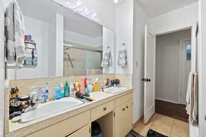 Bathroom with tasteful backsplash, tile patterned floors, a shower with shower door, and vanity