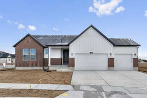 View of front of house with brick siding, board and batten siding, roof with shingles, a garage, and driveway