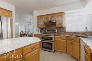 Kitchen featuring sink, backsplash, hanging light fixtures, stainless steel appliances, and light stone countertops