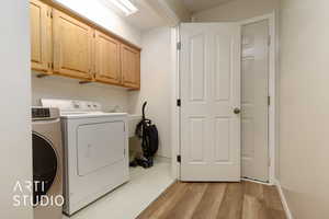 Laundry room with cabinets, light hardwood / wood-style floors, and washing machine and dryer