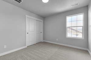 Unfurnished bedroom featuring a textured ceiling, baseboards, visible vents, and light carpet