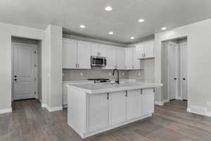 Kitchen with visible vents, a sink, stainless steel microwave, wood finished floors, and light countertops
