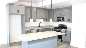 Kitchen with a kitchen island, appliances with stainless steel finishes, gray cabinetry, and decorative light fixtures