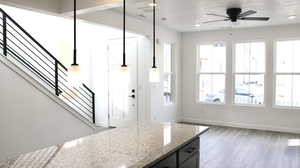 Kitchen with hanging light fixtures, wood-type flooring, light stone countertops, and ceiling fan