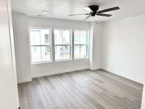 Empty room featuring ceiling fan, a textured ceiling, and light hardwood / wood-style floors