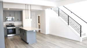 Kitchen with hanging light fixtures, appliances with stainless steel finishes, a center island, and gray cabinets