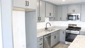 Kitchen with sink, gray cabinets, stainless steel appliances, light stone counters, and light wood-type flooring