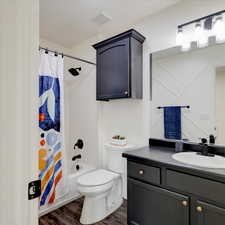 Full bathroom with wood-type flooring, toilet, shower / bath combo with shower curtain, and vanity