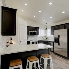 Kitchen featuring pendant lighting, sink, appliances with stainless steel finishes, tasteful backsplash, and vaulted ceiling