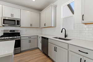 Kitchen with sink, white cabinetry, light hardwood / wood-style flooring, appliances with stainless steel finishes, and backsplash