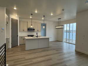 Kitchen with an island with sink, sink, hanging light fixtures, stainless steel appliances, and a water view