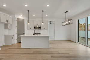 Kitchen with pendant lighting, white cabinetry, range, and an island with sink