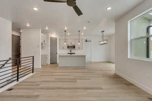 Unfurnished living room with sink, ceiling fan with notable chandelier, and light hardwood / wood-style floors