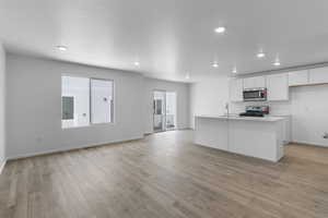 Kitchen with sink, light hardwood / wood-style flooring, appliances with stainless steel finishes, a kitchen island with sink, and white cabinets