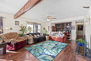 Living room with beam ceiling, dark wood-type flooring, built in features, and ceiling fan