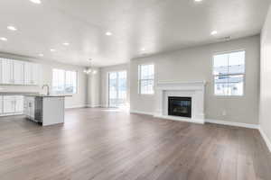 Unfurnished living room featuring an inviting chandelier, sink, light hardwood / wood-style flooring, and a textured ceiling