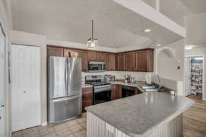 Kitchen with pendant lighting, sink, light tile patterned floors, kitchen peninsula, and stainless steel appliances