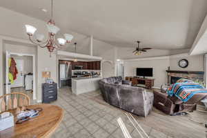 Living room with lofted ceiling, light tile patterned floors, ceiling fan with notable chandelier, and a fireplace