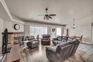 Living room with lofted ceiling, wood-type flooring, a textured ceiling, a fireplace, and ceiling fan with notable chandelier