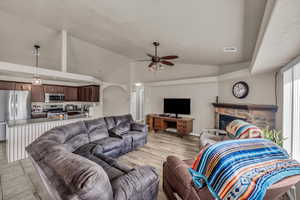 Living room with a fireplace, ceiling fan, and vaulted ceiling