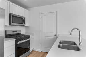 Kitchen with appliances with stainless steel finishes, sink, white cabinets, and light hardwood / wood-style floors