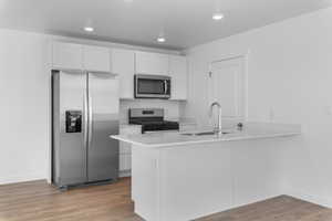 Kitchen with white cabinetry, stainless steel appliances, kitchen peninsula, and sink