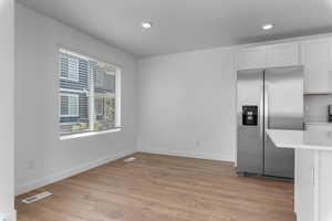 Kitchen featuring stainless steel fridge with ice dispenser, white cabinets, and light wood-type flooring