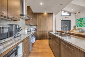 Kitchen with wall chimney exhaust hood, sink, light wood-type flooring, pendant lighting, and stainless steel appliances