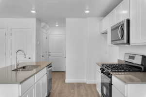 Kitchen featuring sink, a textured ceiling, laminate flooring, stainless steel appliances, and white cabinets