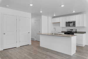 Kitchen featuring sink, stainless steel appliances, an island with sink, and white cabinets