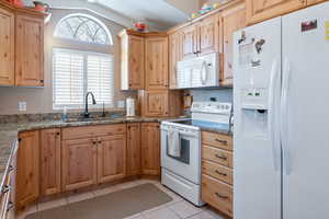 Kitchen with sink, stone countertops, vaulted ceiling, light tile patterned floors, and white appliances