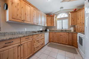 Kitchen with stone counters, lofted ceiling, sink, and white appliances