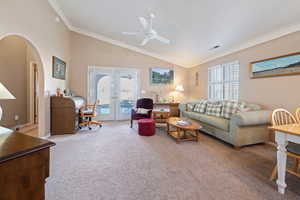 Carpeted living room featuring vaulted ceiling, ceiling fan, crown molding, and french doors