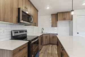 Kitchen with sink, light hardwood / wood-style flooring, backsplash, stainless steel appliances, and decorative light fixtures